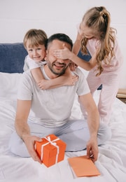 A girl puts her hands over dad's eyes as she and her bother give him a surpirse father's day gift.