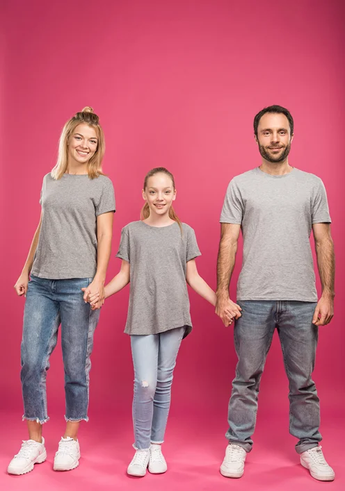 Parents holding had with their tween daughter in the middle against a pink backdrop.