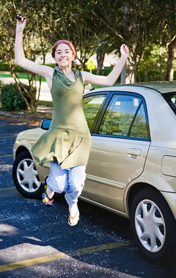 A teen girl is jumping for joy beside her new car.