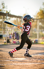 Girl Swinging Bat in Little League Game