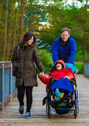 Man and woman pushing child in wheelchair on an outdoor walk.