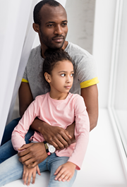 African American dad and daughter sitting on a window sill looking outside.