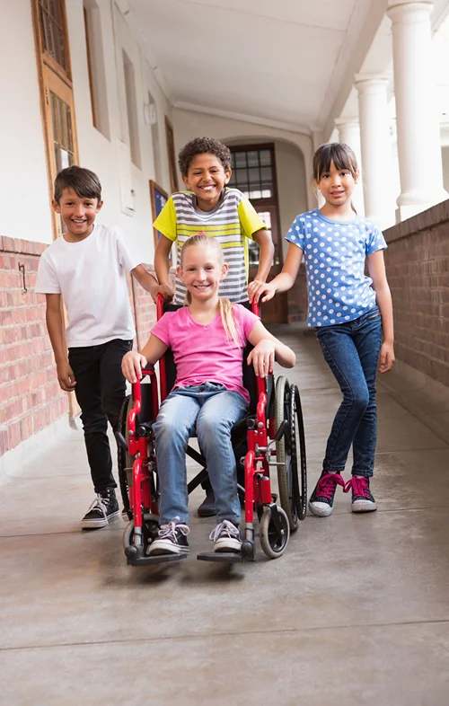 A girl is being pushed in her wheelchair by friends at school.