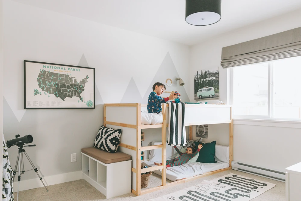 A boy in his bedroom on top bunk of a loft bed.