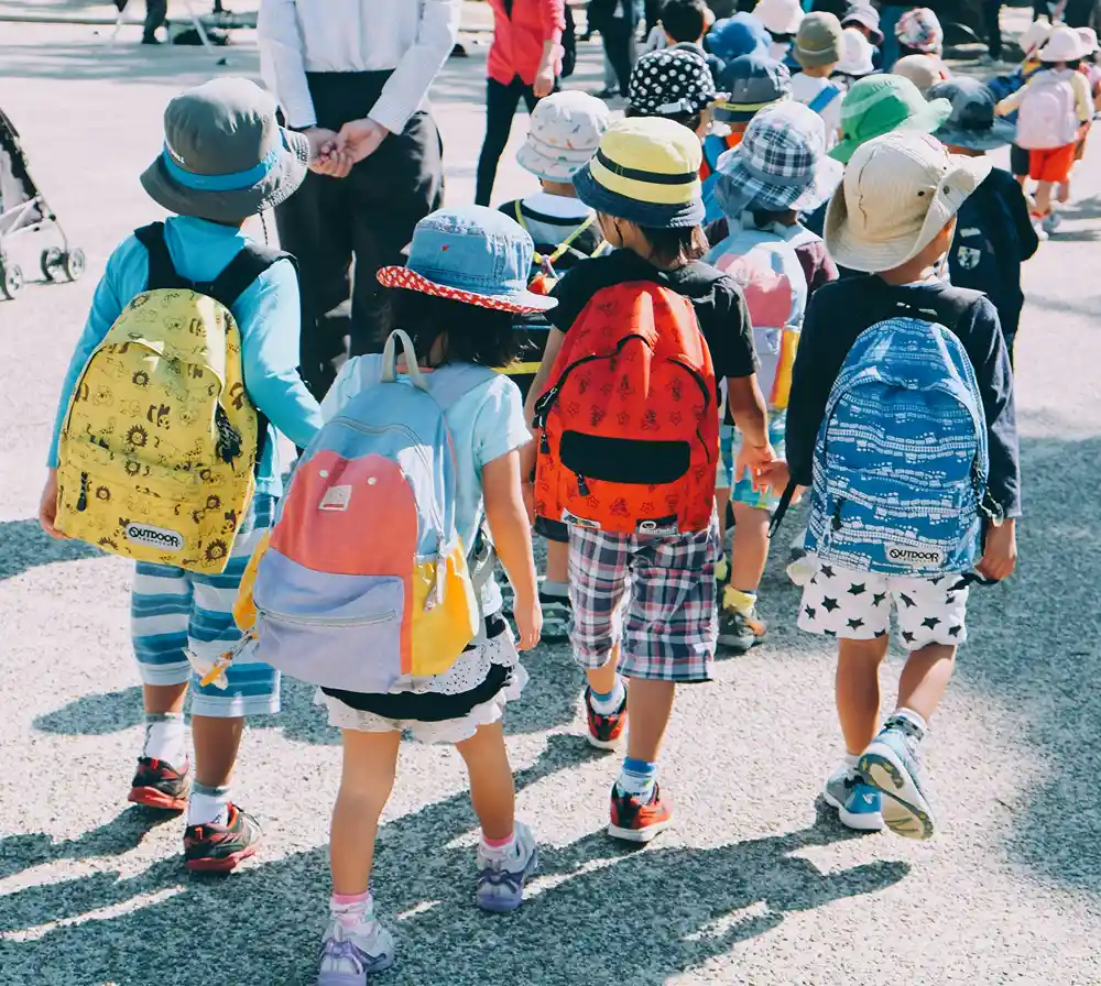 A group of kids in backpacks walking in a line to school.