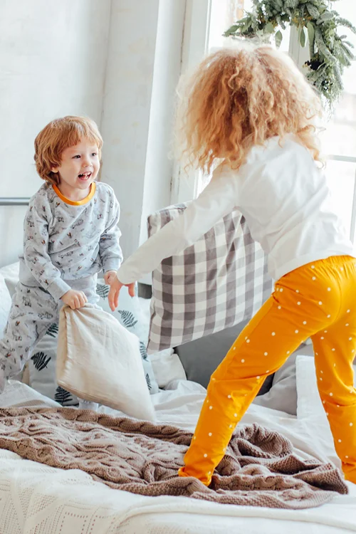 Boy and Girl having a pillow fight on a bed.