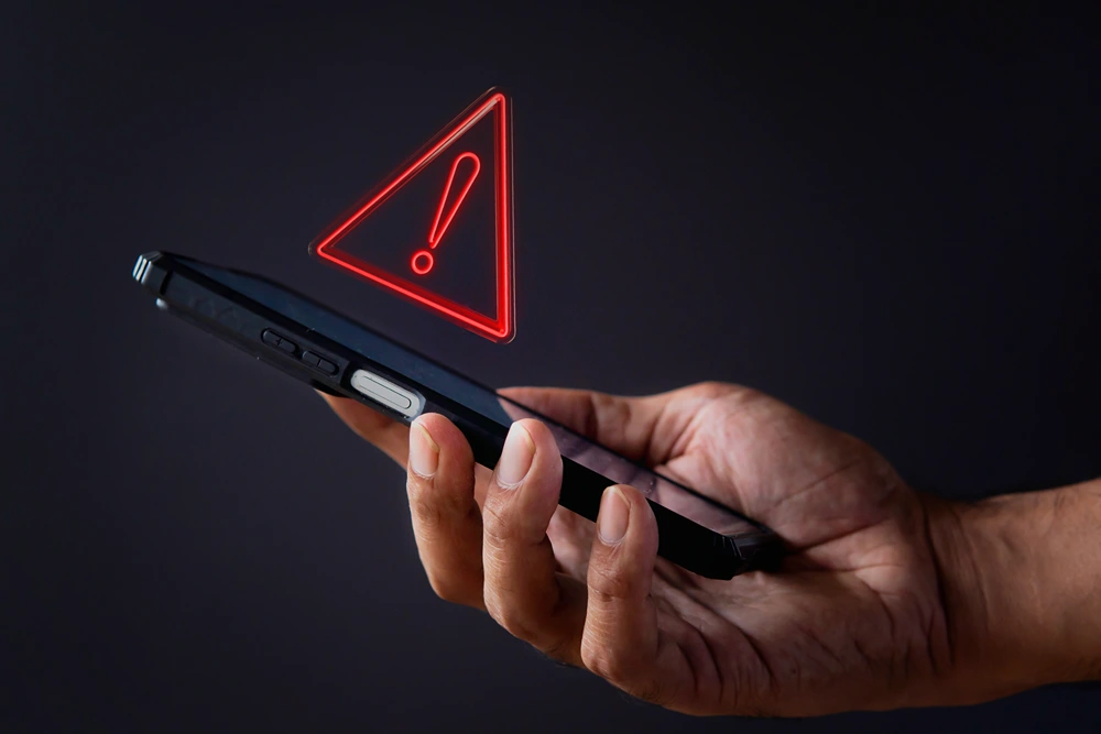 Man holds smartphone with hovering danger sign above it.