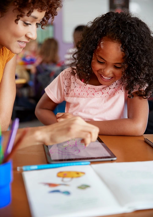 A women is working with a child on a table with open notebook beside.