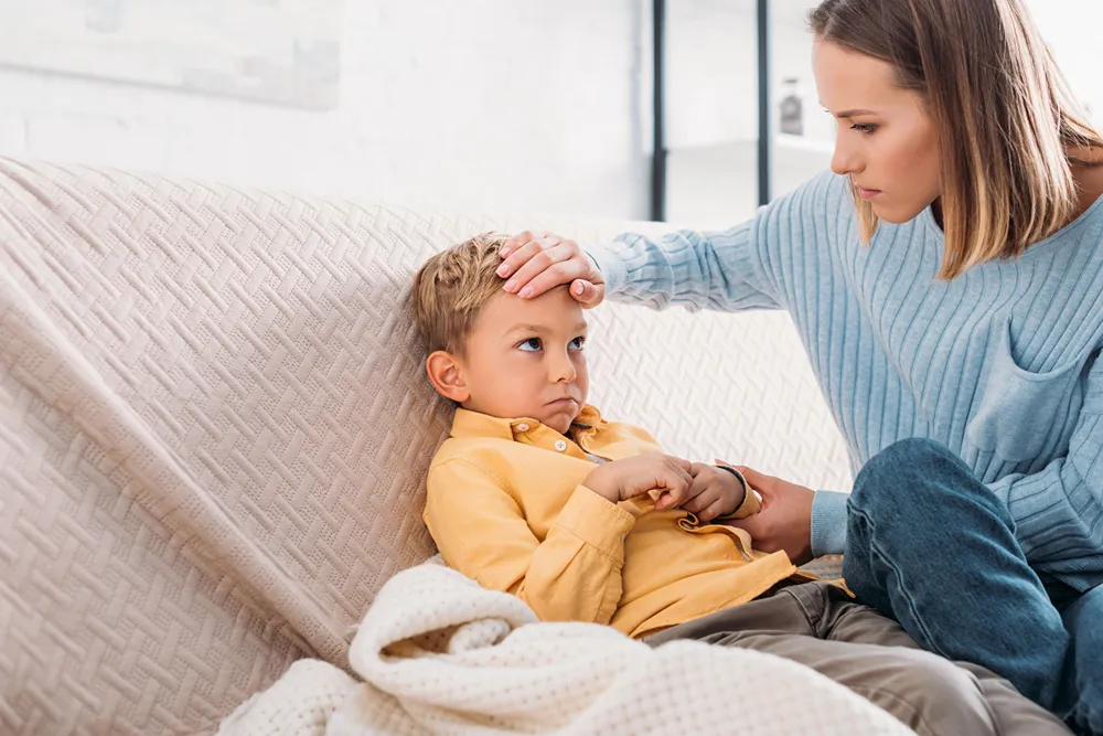 Mom puts hand on her son's forehead as he holds his tummy.