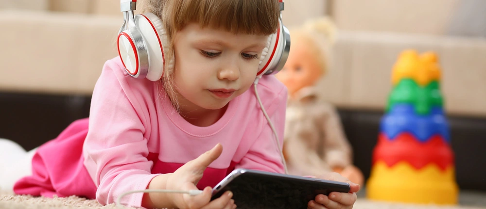 A little listens to an audiobook on headphones while following along on her kindle.