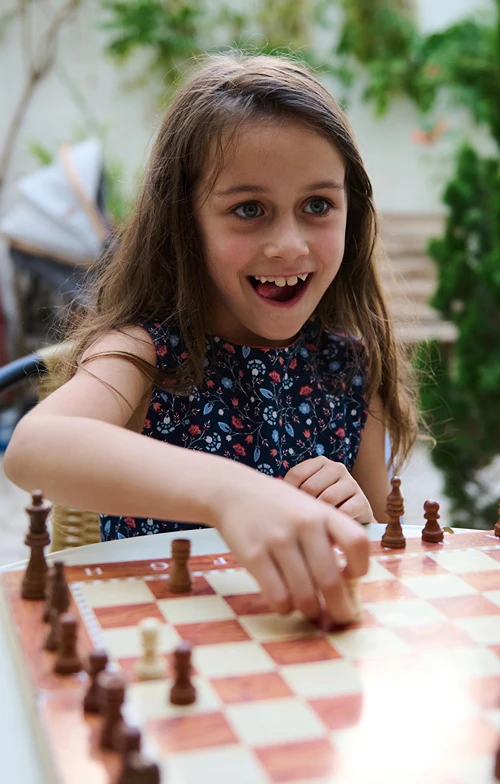 Girl playing chess with someone and smiling as she makes a bold chess move.