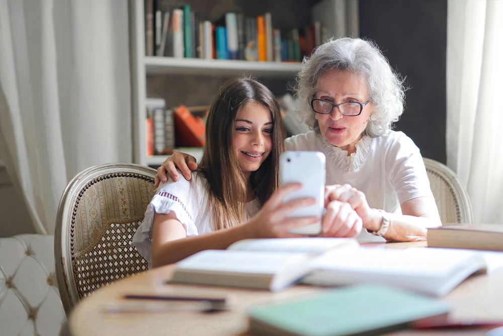 A girl is holding up her phone and showing her grandmother something on the screen.