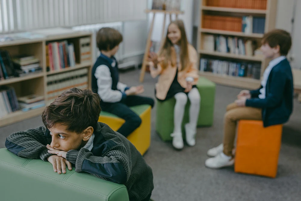 A forlorn student sits in the forefront as classmates talke behind him.