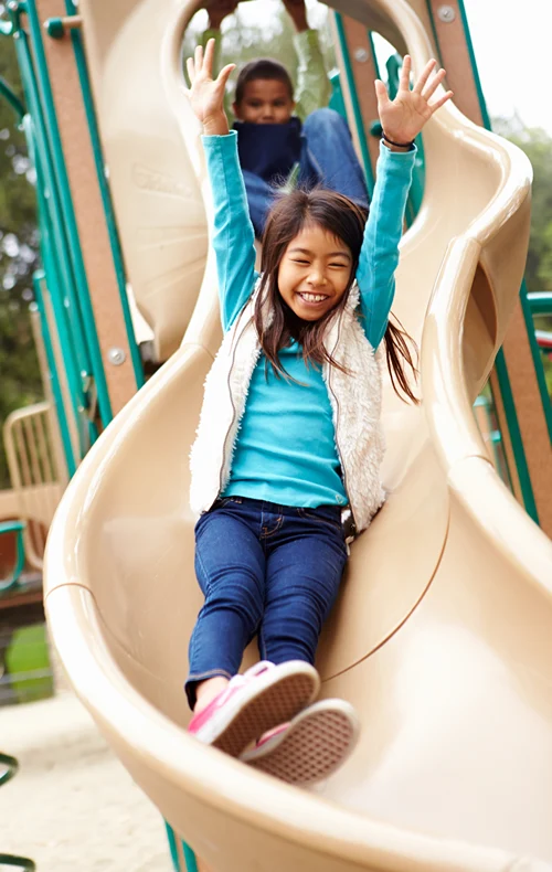 Kids sliding down a squiggly slide in a playground.
