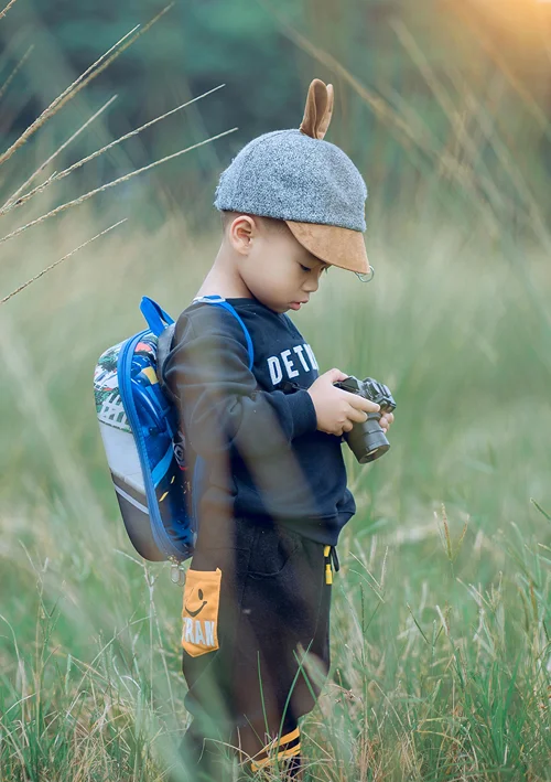 A toddler with a hat holding a camera in a field.
