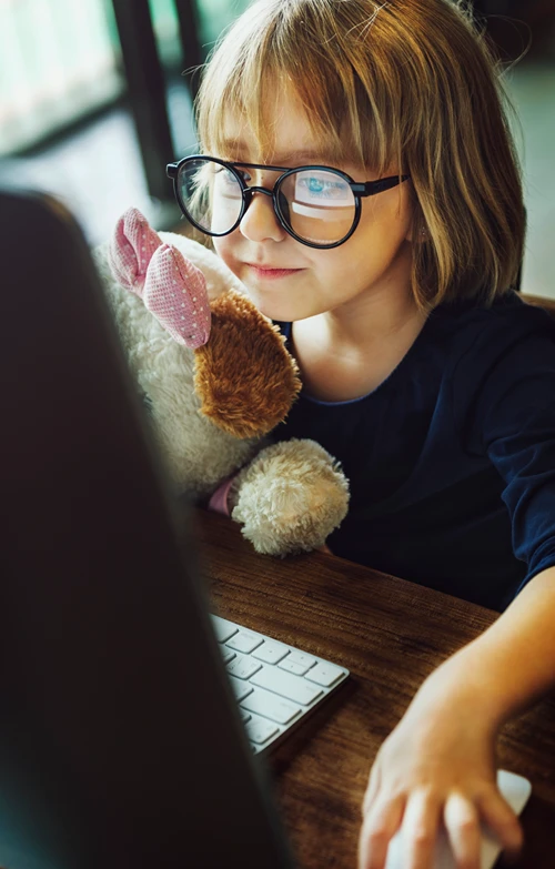 A little girl holding a stuffed animal as she browses the internet on a disktop computer.