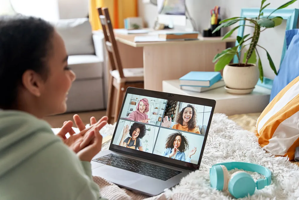 A tween girl with a laptop showing 4 friends on the screen in group chat.
