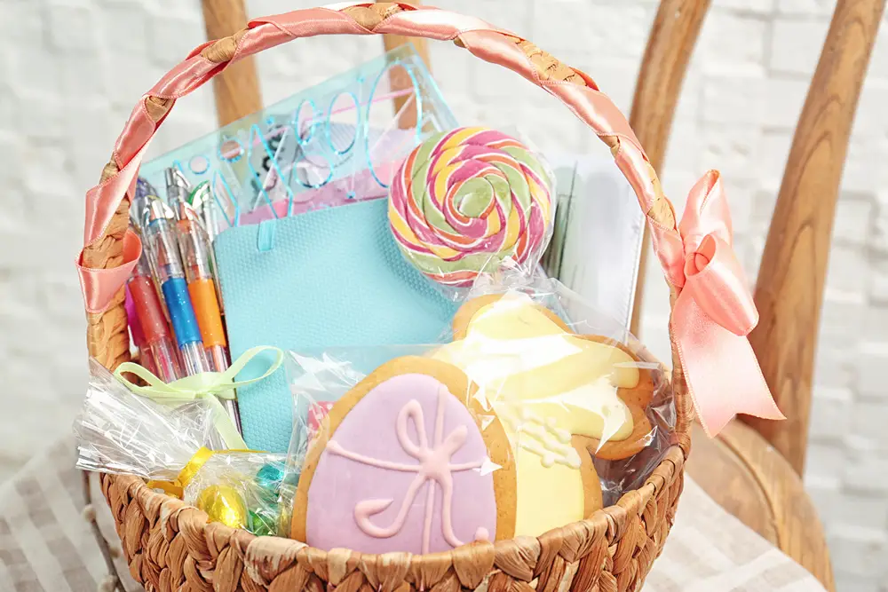 A gift basket filled with candy, a sucker, colorful pens, and notebook.