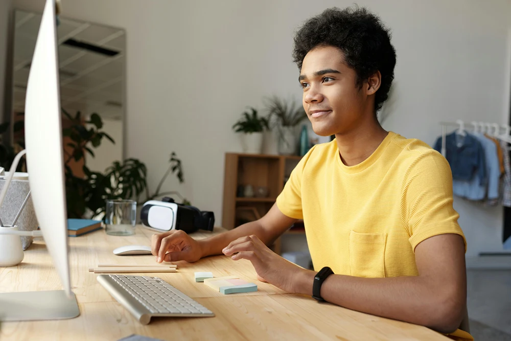 A male teen is browsing the web on a computer at home.
