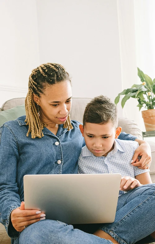 Laptop on mother's lap as she shows it to her son.
