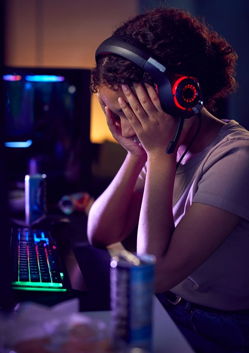 A troubled teen with hands over her face while gaming