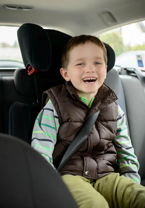 A boy with autism smiling from his car seat.