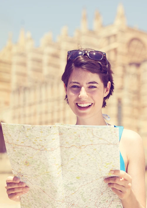 Happy young woman holding a paper map with both hands.