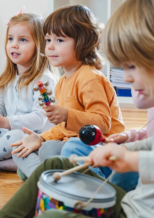 A group of preschoolers playing musical instruments while sitting on the floor.