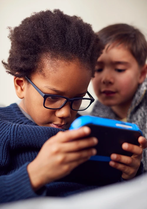 Boy gaming on hand held device as his friend watches.