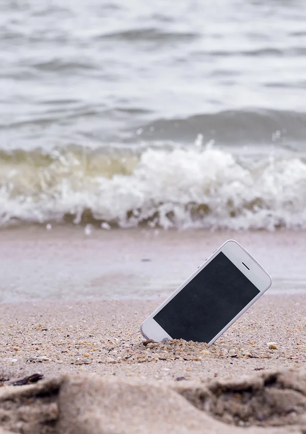 A phone sticking out of the sand on a beach as the tide rises.