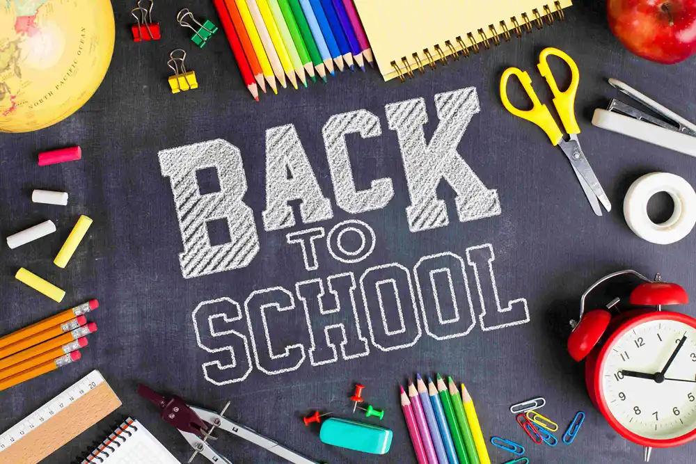 Back to School written on black board surrounded by school supplies.