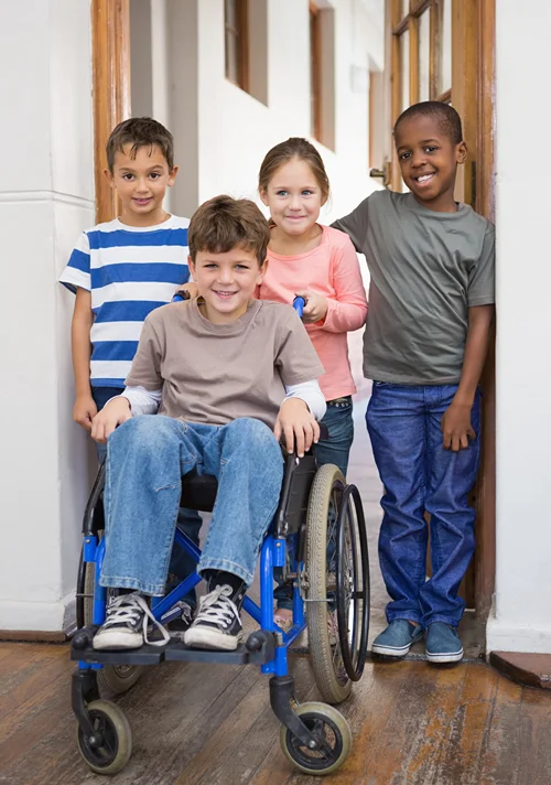 Boy is pushed in his wheelchair by a group of friends.