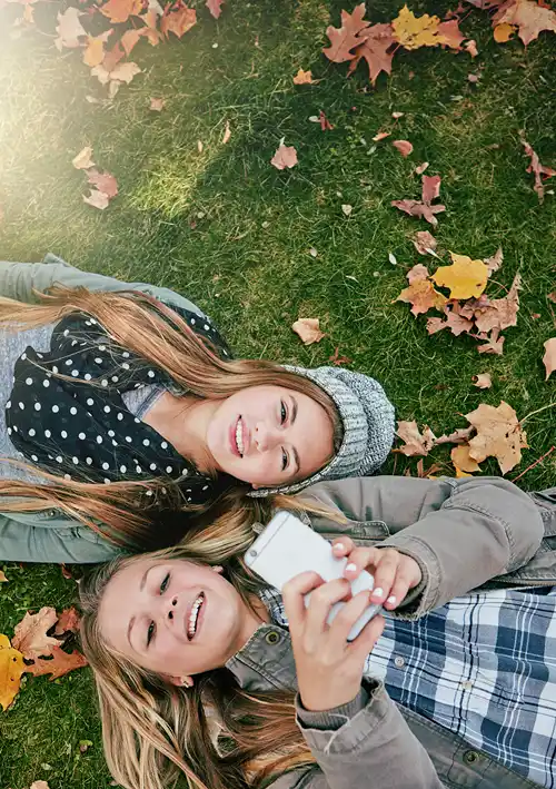 Two girls laying on grass looking up a smartphone.