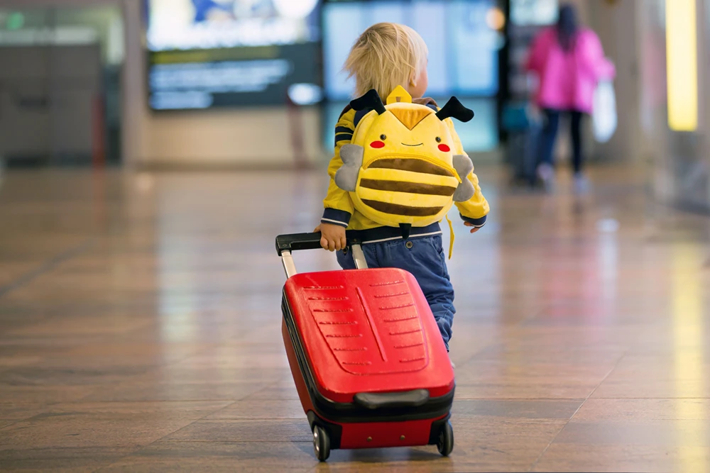 A toddler with backpack and suitcase in airport.
