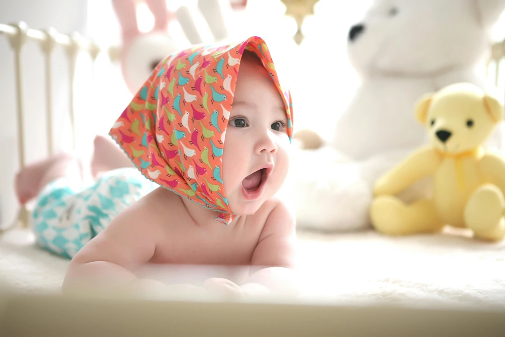 Baby on stomach in crib with wide open mouth as if trying to talk.