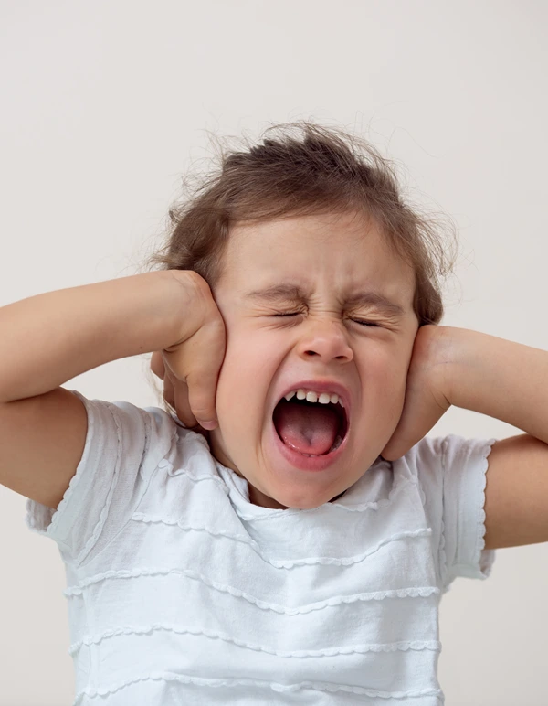 A little girl holds her hands over her ears and screams.