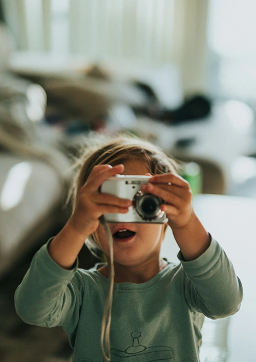 Young child playing pretending to take a picture with a camera.