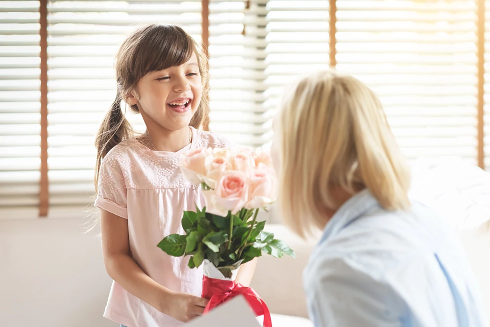A girl smiles as she give mom a bouquet of beautiful pink roses.