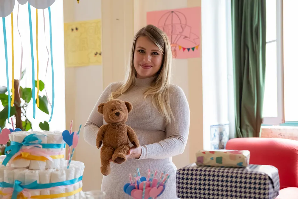 Woman holding teddy bear surrounded by wrapped gifts.