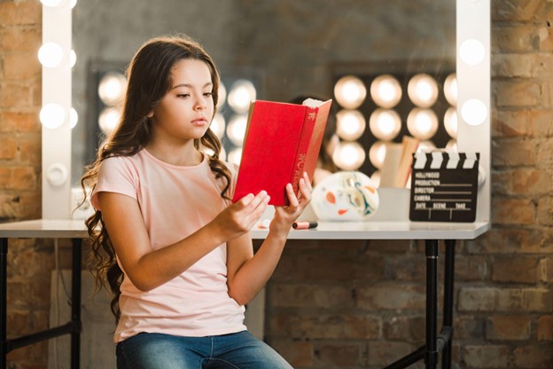 Pretty girl reading a book in front of a dressing mirror and table. 