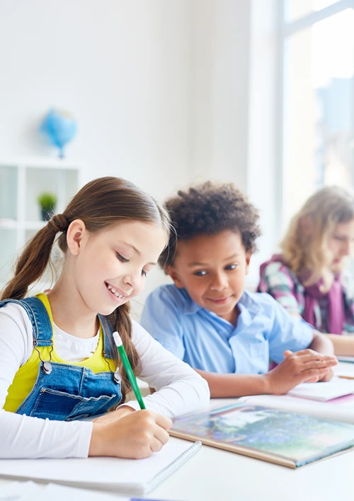Kids working in a row on a table in school classroom.