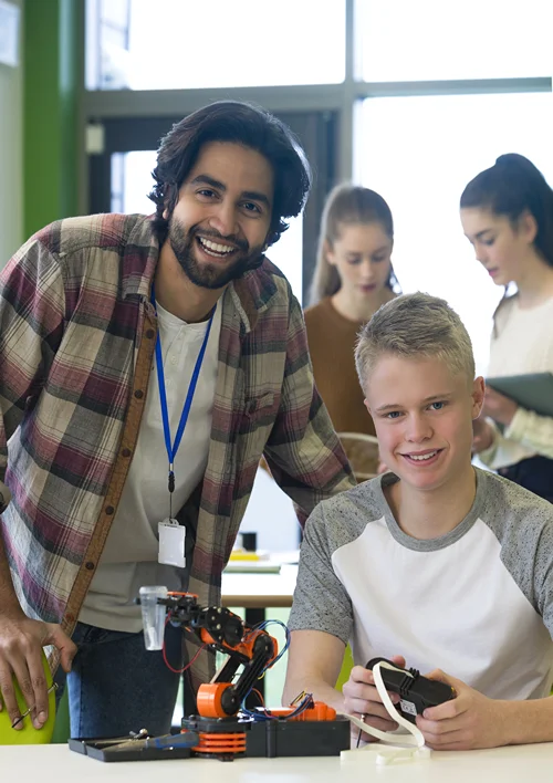 A teacher in STEM classroom helping boy with project.