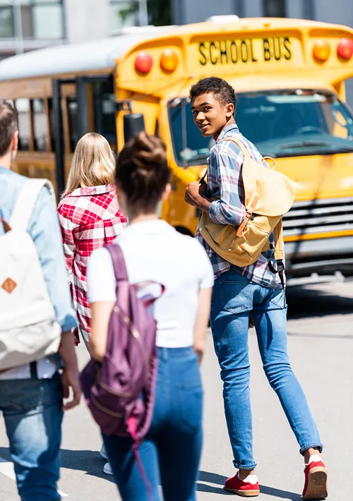 Teen boy waves back as he walks to the school bus with other students.