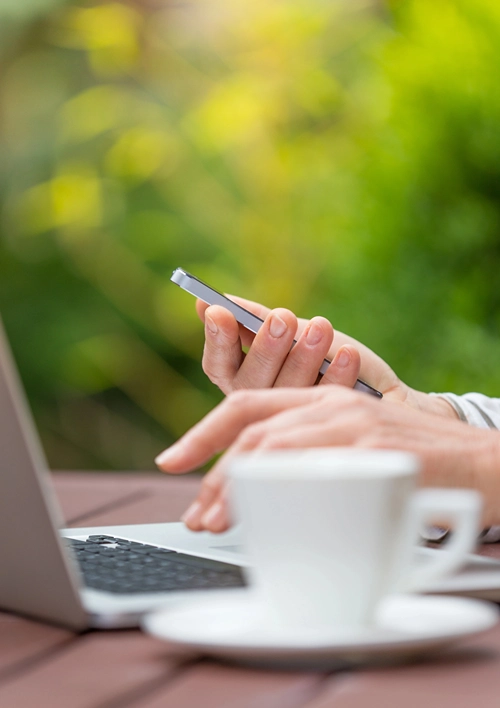 Woman typing on laptop and looking at phone while on coffee break.