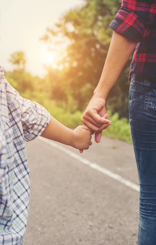 A little boy holds on to his mom's finger as they walk along a path.