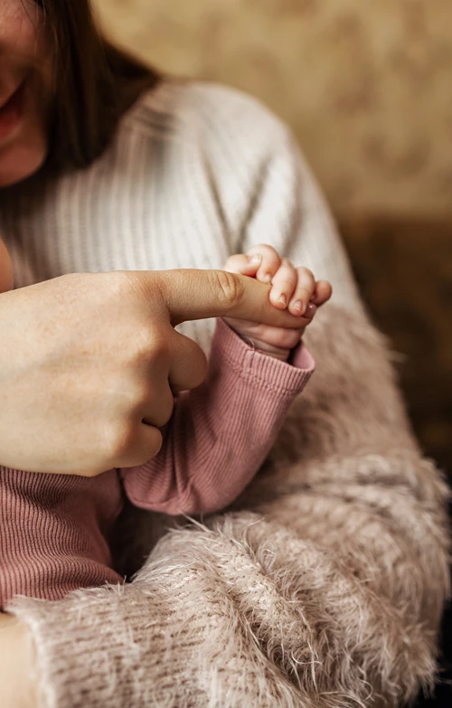 Mom hold's baby as baby holds her finder