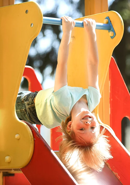 Smiling boy hanging upside down on play ground bar.