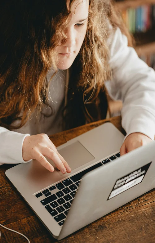 A red headed girl sits at a desk intently on her laptop.