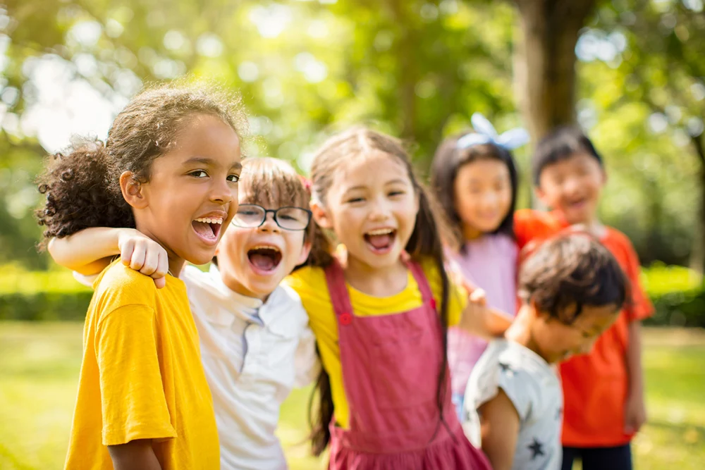 Kids arm in arm smiling in a park.