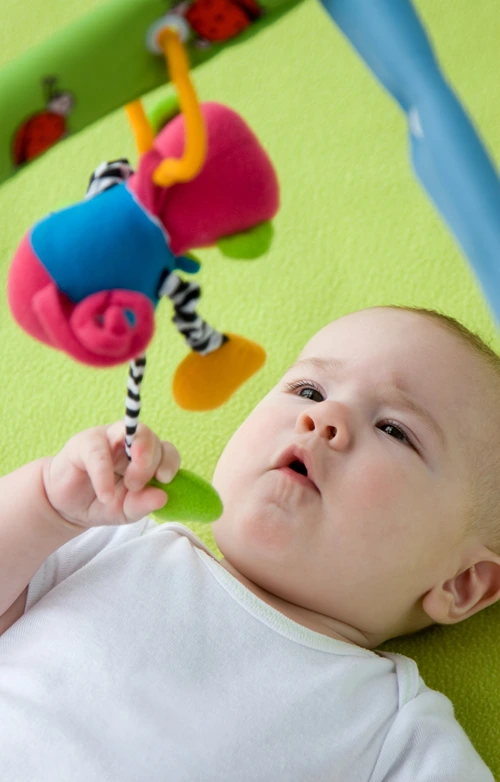 Baby in crib playing with hanging toy.